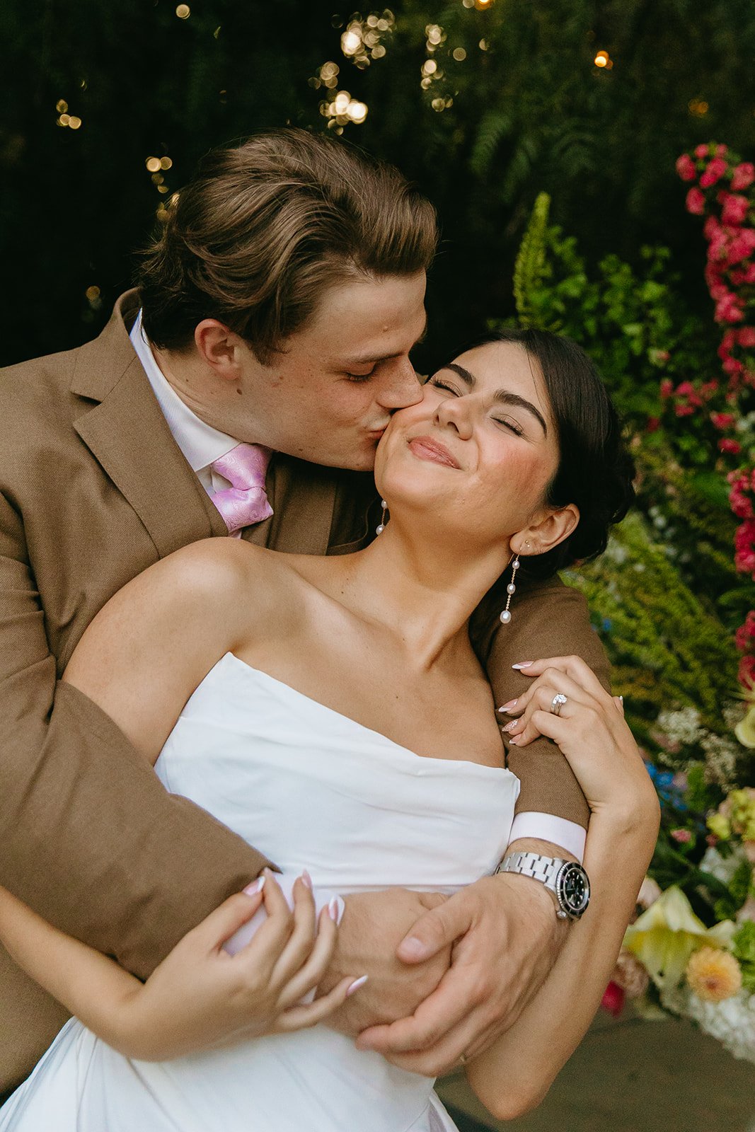 A groom kissing a bride on the cheek for wedding photos