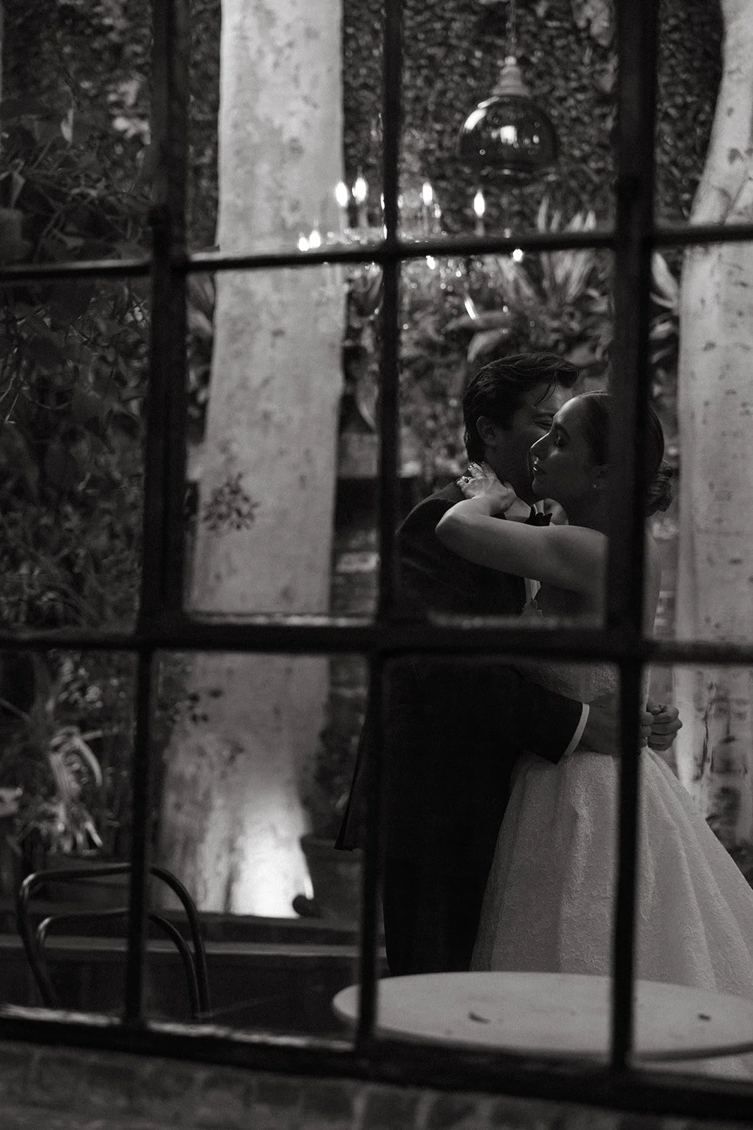 A bride and groom seen kissing through a window