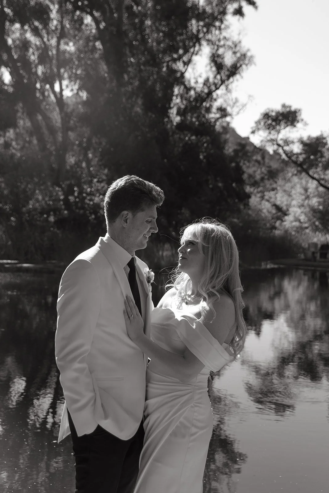 A black and white photo of a bride and groom in front of a pond