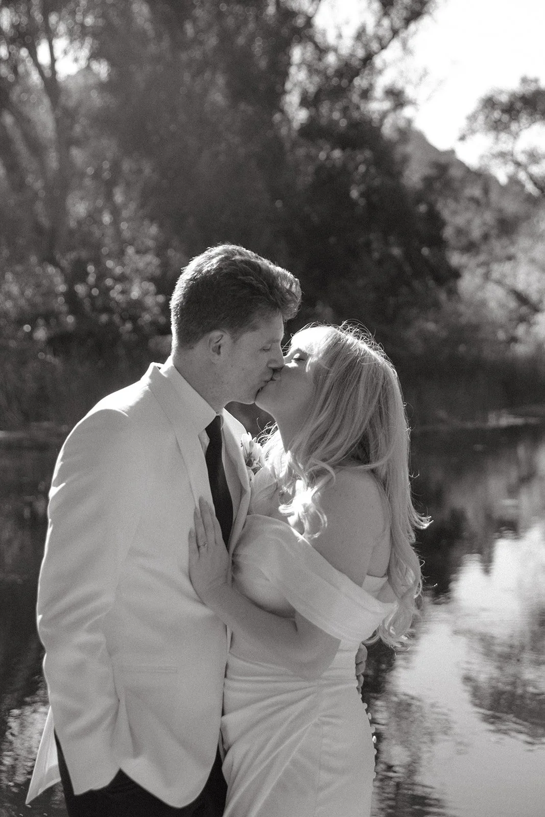 A black and white photo of a bride and groom in front of a pond