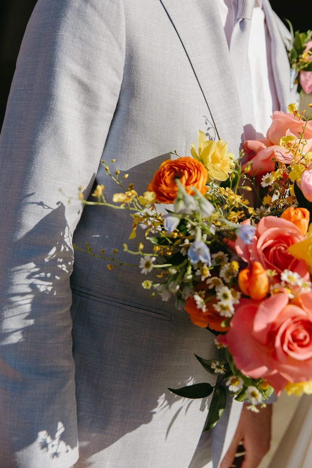 A colorful wedding bouquet against a groom's blue suit