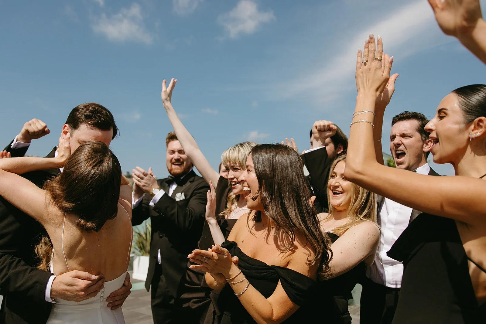 A wedding party cheering while a bride and groom kiss