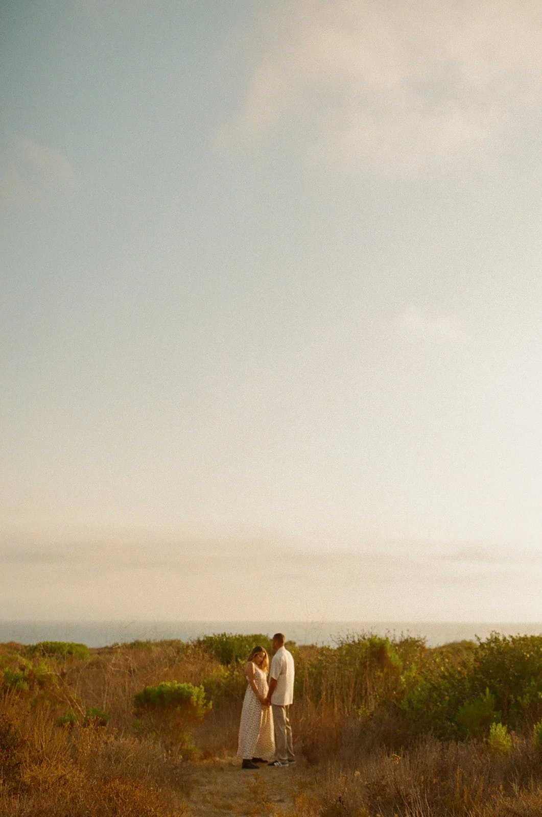 A couple posing for engagement photos on a trail to the beach