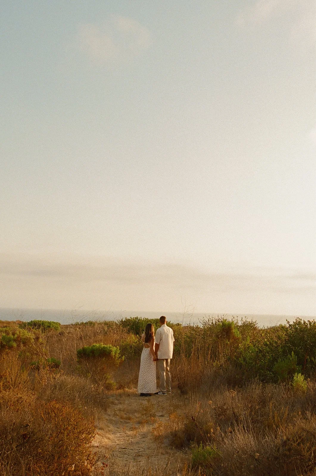 A couple posing for engagement photos on a trail to the beach