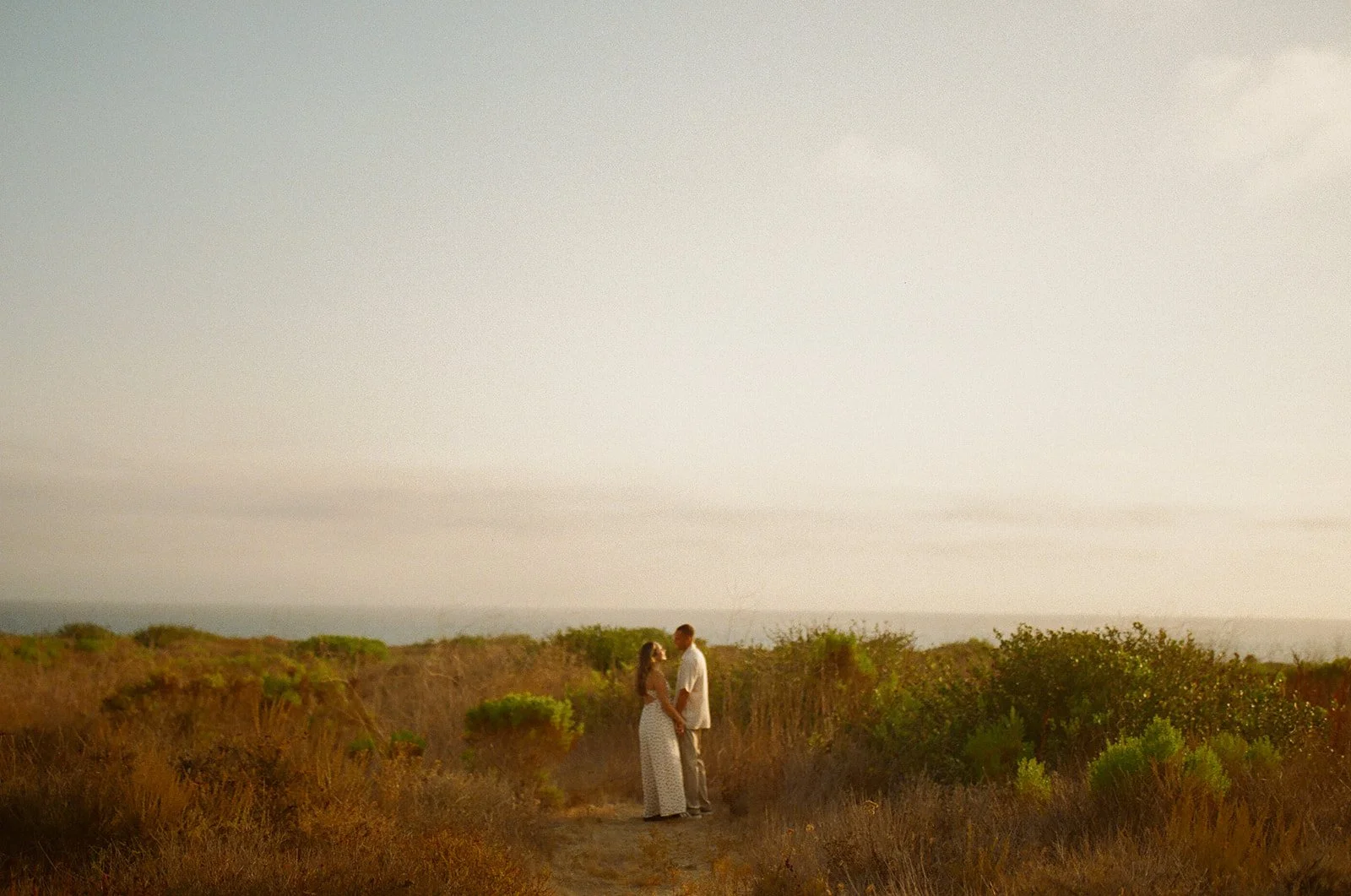A couple standing in a field showing what to wear for engagement photos