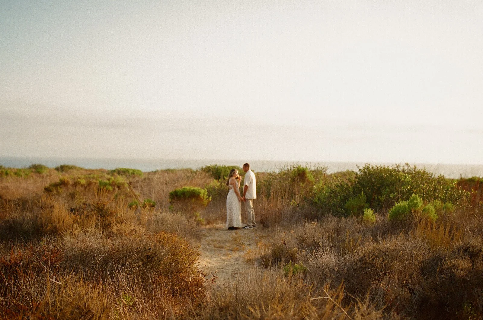 A couple standing in a field showing what to wear for engagement photos