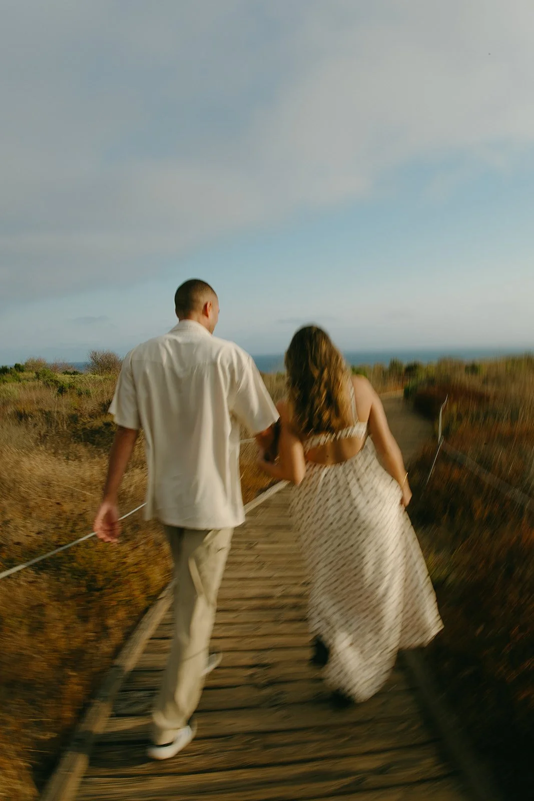 A couple walking down a path towards the beach in their beach engagement photo outfits