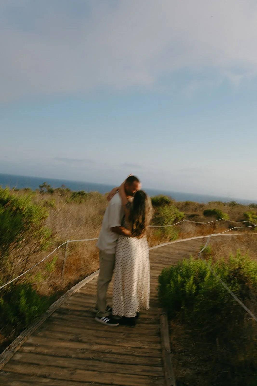 A couple walking down a path towards the beach in their beach engagement photo outfits