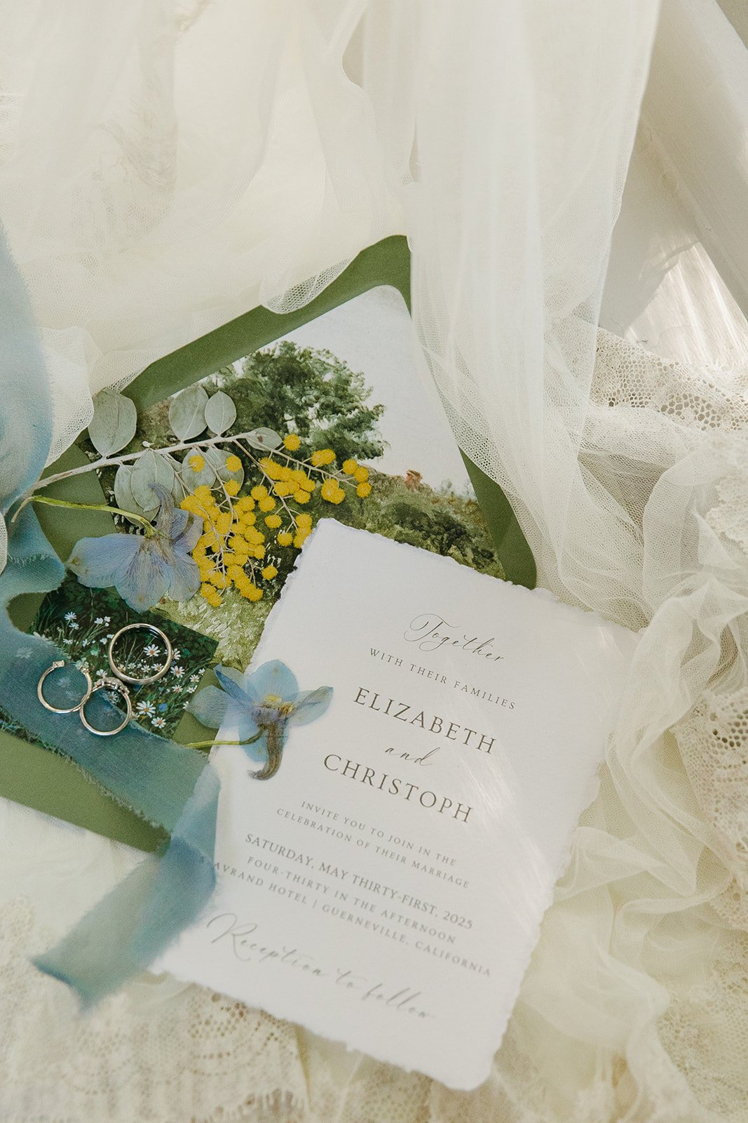 A wedding flat lay with ribbon, wedding invitations, and rings
