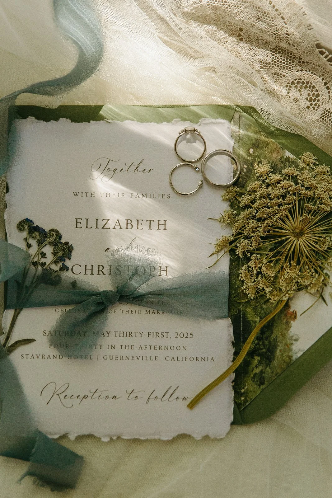 A wedding flat lay with ribbon, wedding invitations, and rings