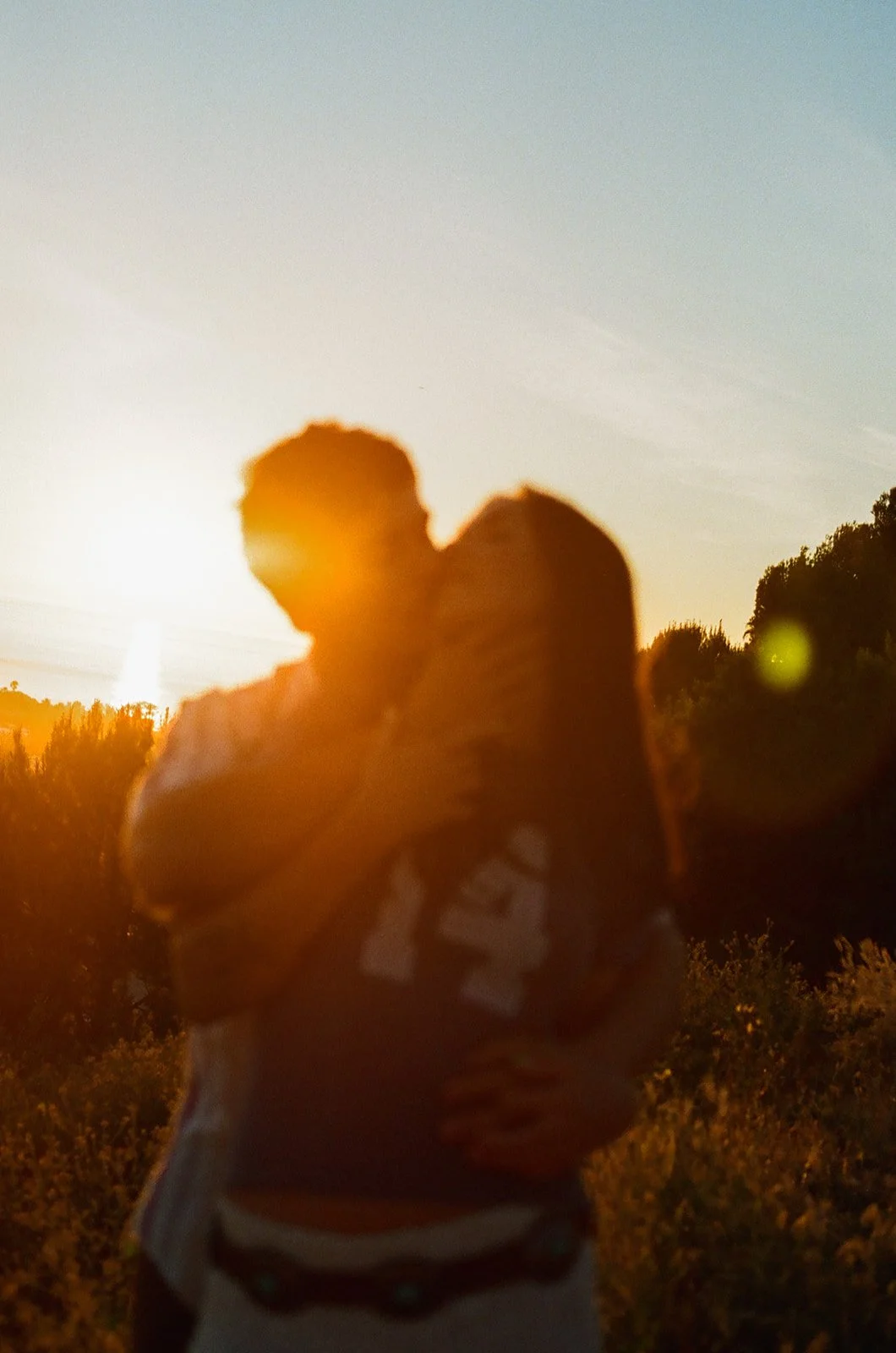 A couple posing for film engagement photos with the sun hitting behind them