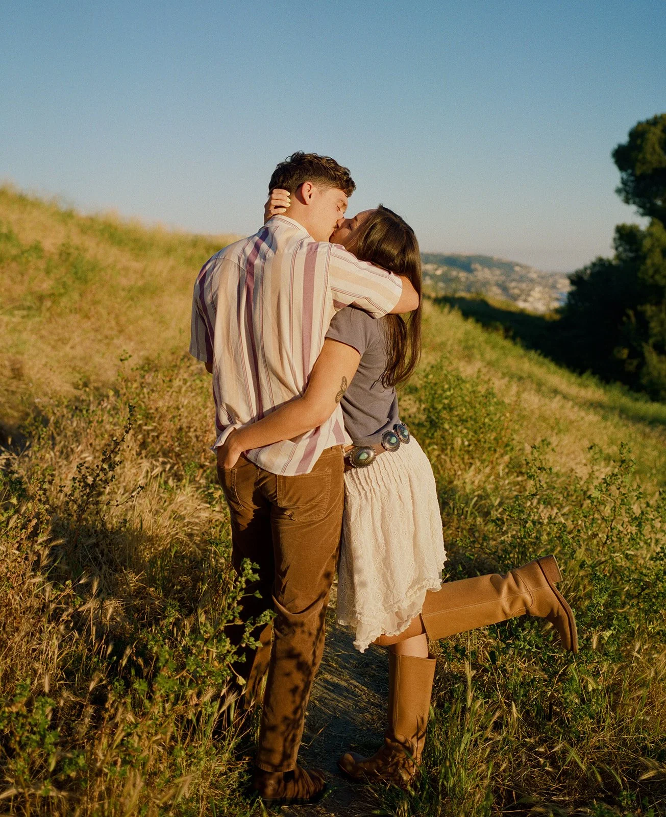 A couple kissing in film engagement photos in a field