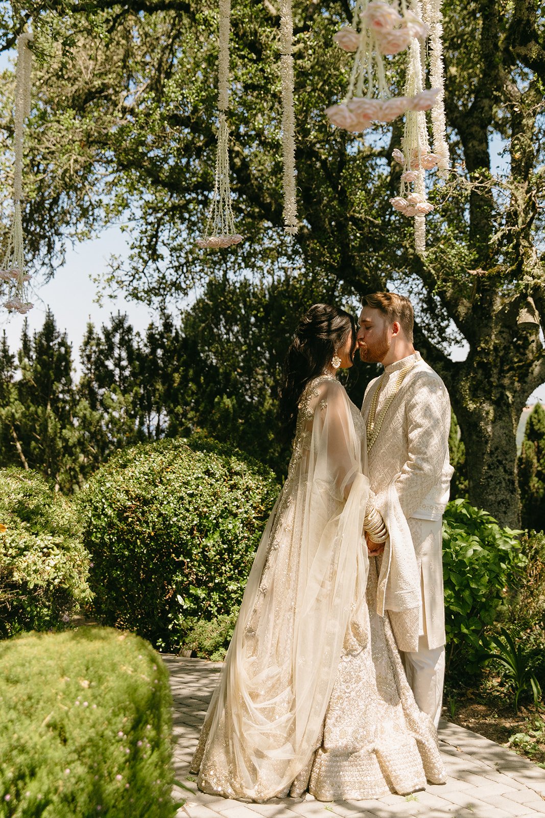 Bride and groom sharing a quiet moment in a lush garden, surrounded by greenery, soft sunlight, and delicate floral installations.