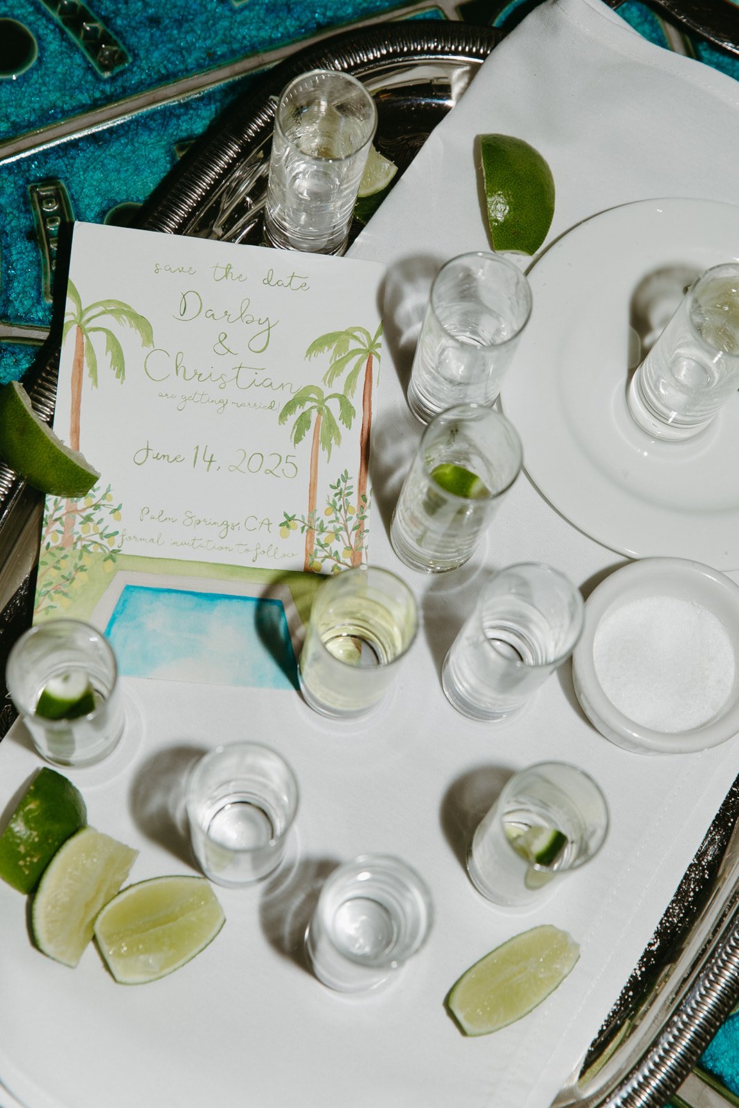 A wedding flat lay with wedding invitations and tequila shots