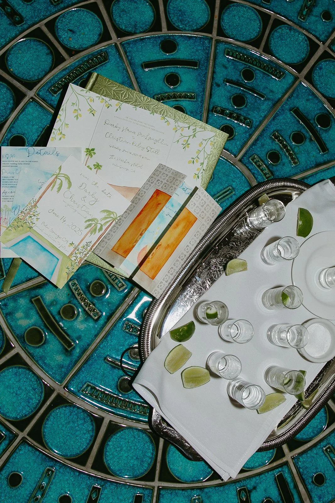 A wedding flat lay with wedding invitations and tequila shots