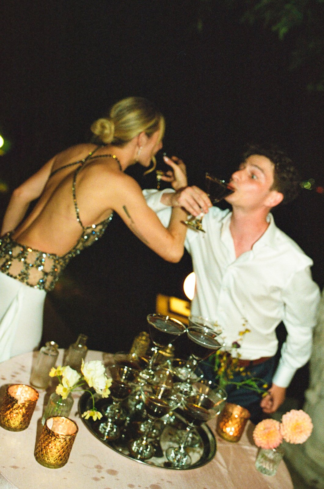 A bride and groom drinking from a martini tower at their wedding