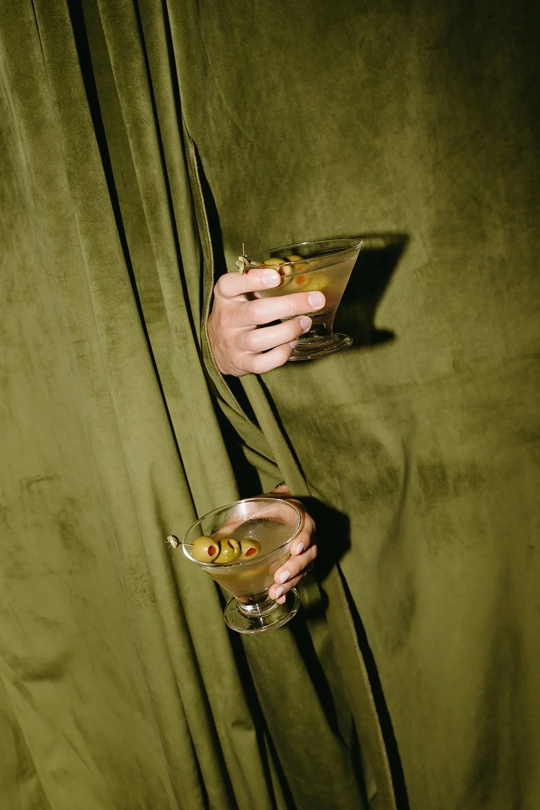 A unique wedding photo with a wedding couple holding drinks out of a curtain