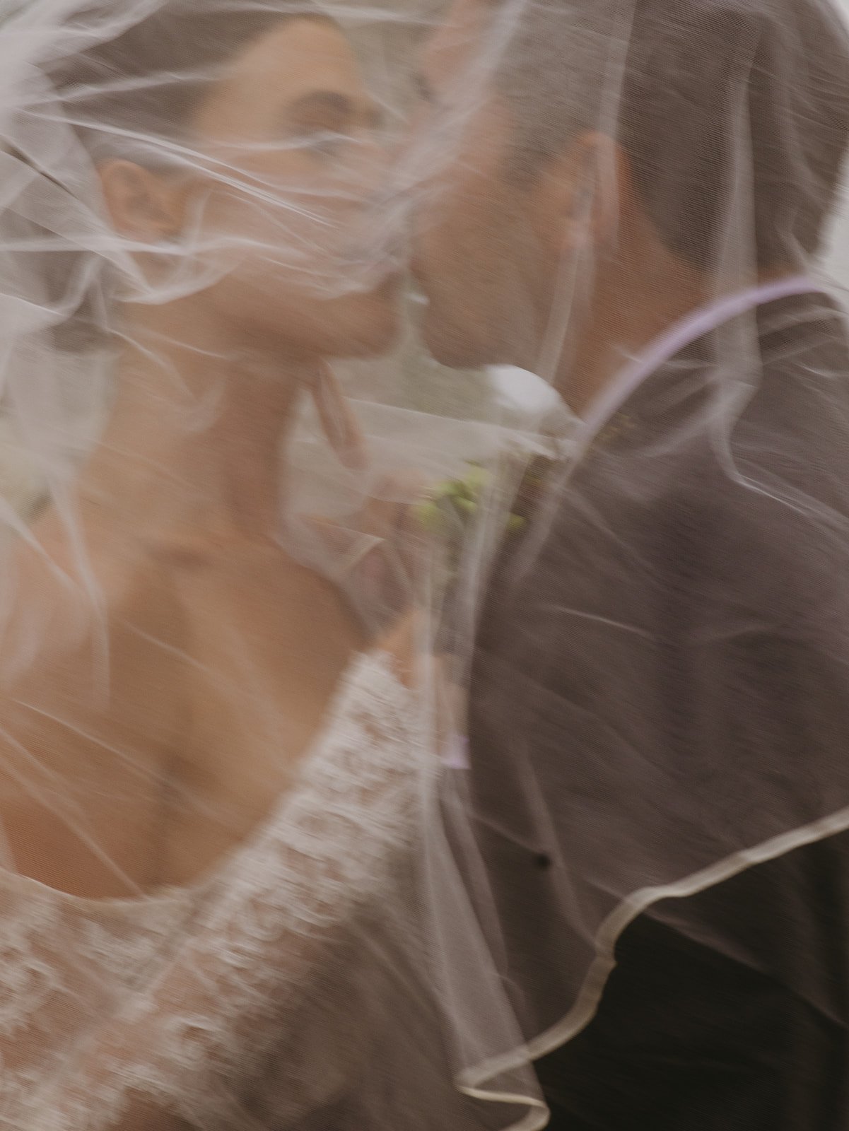 A bride and groom taking wedding portraits underneath a veil