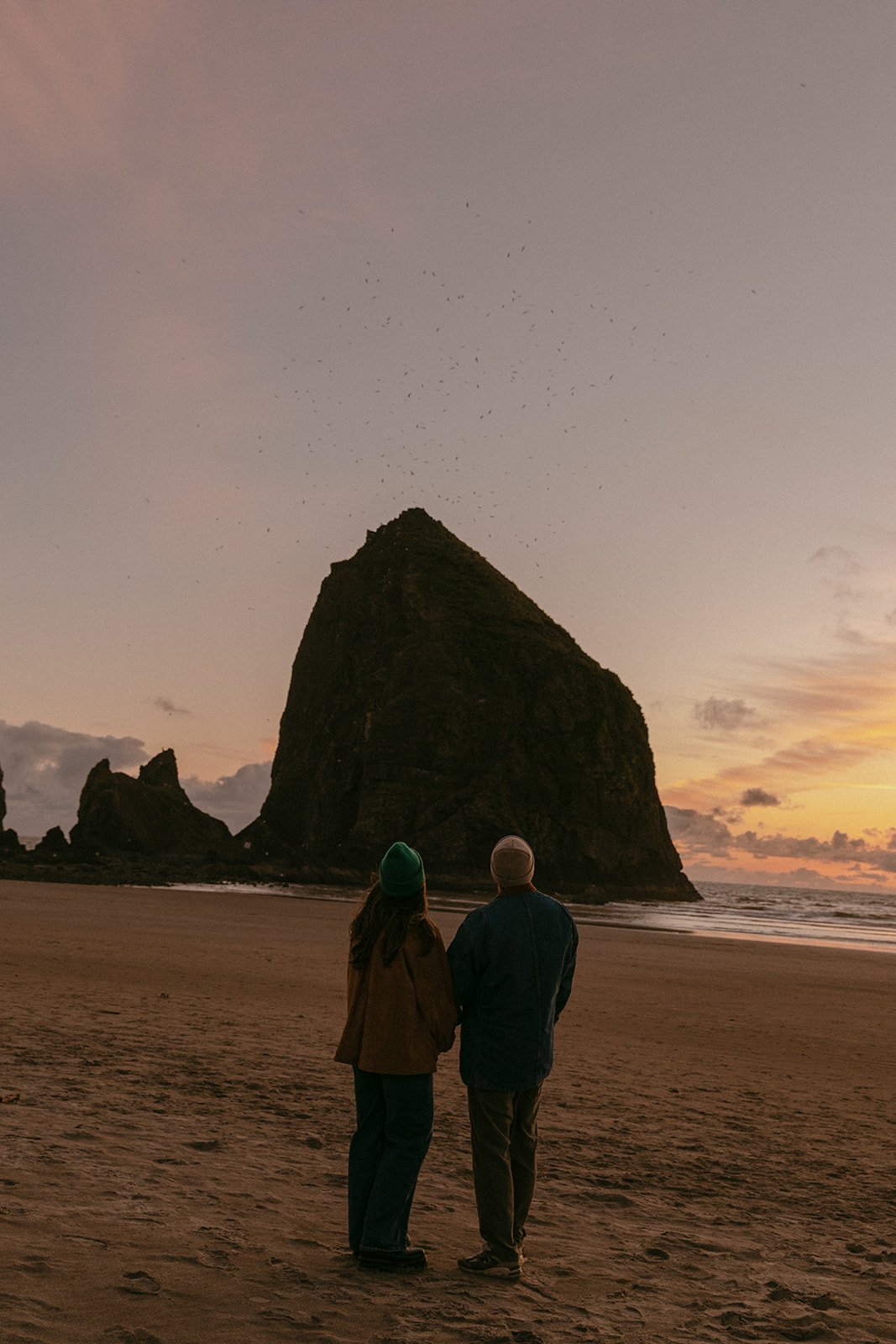 A couple taking sunset engagement photos on cannon beach