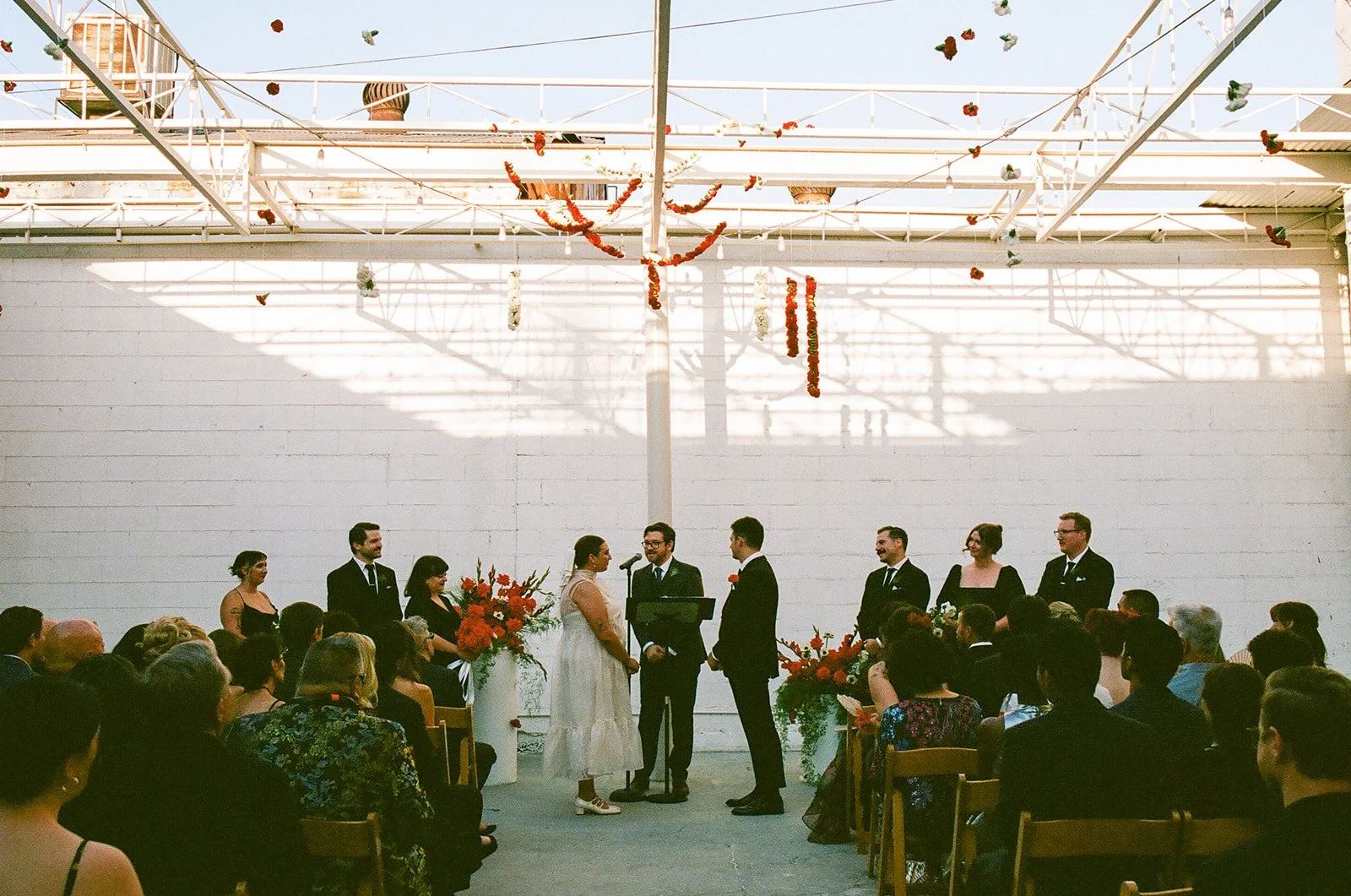 The couple standing at the altar during their ceremony at The Revery LA, surrounded by their wedding party and guests beneath hanging floral installations.