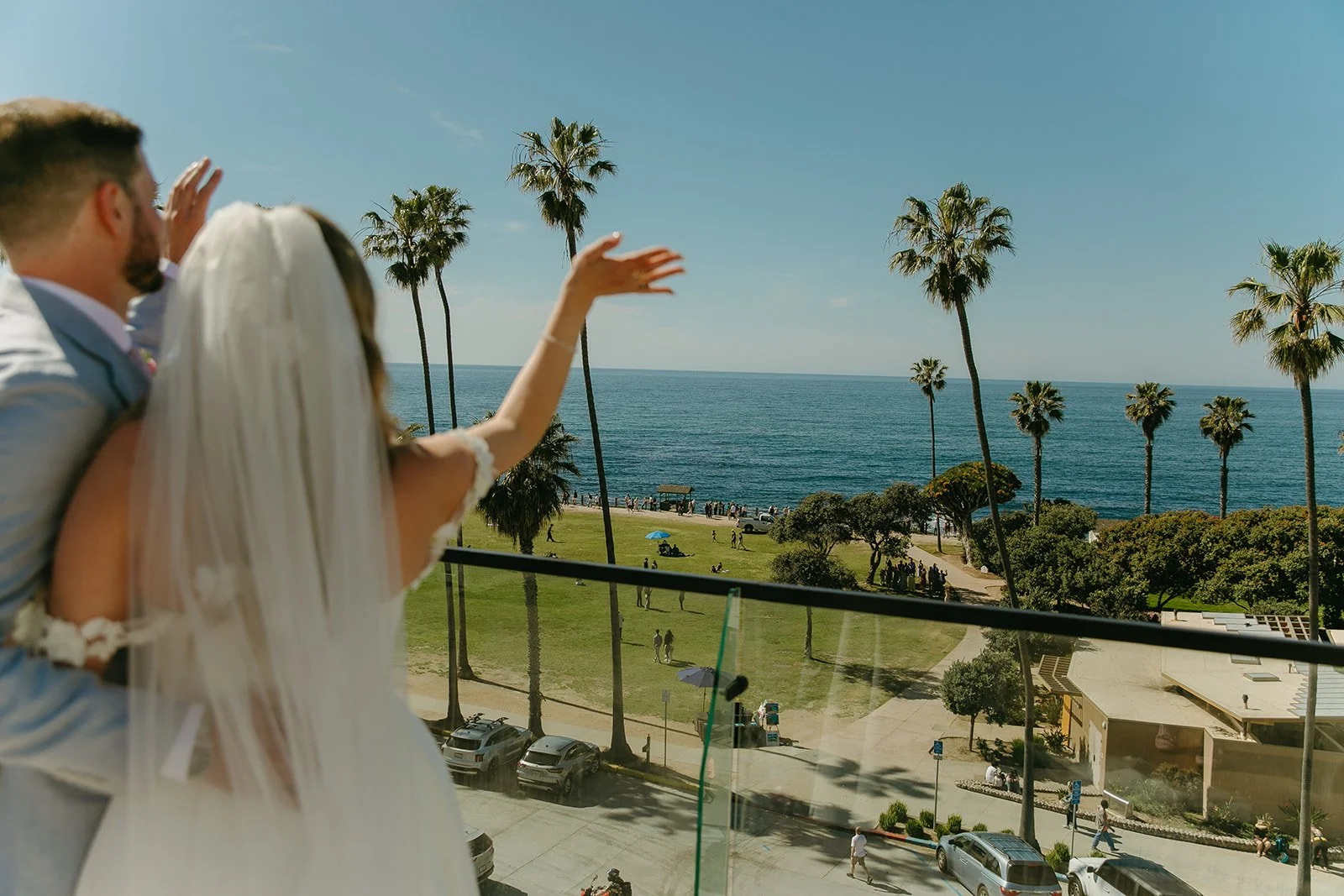 A bride and groom waving at wedding guests from a rooftop