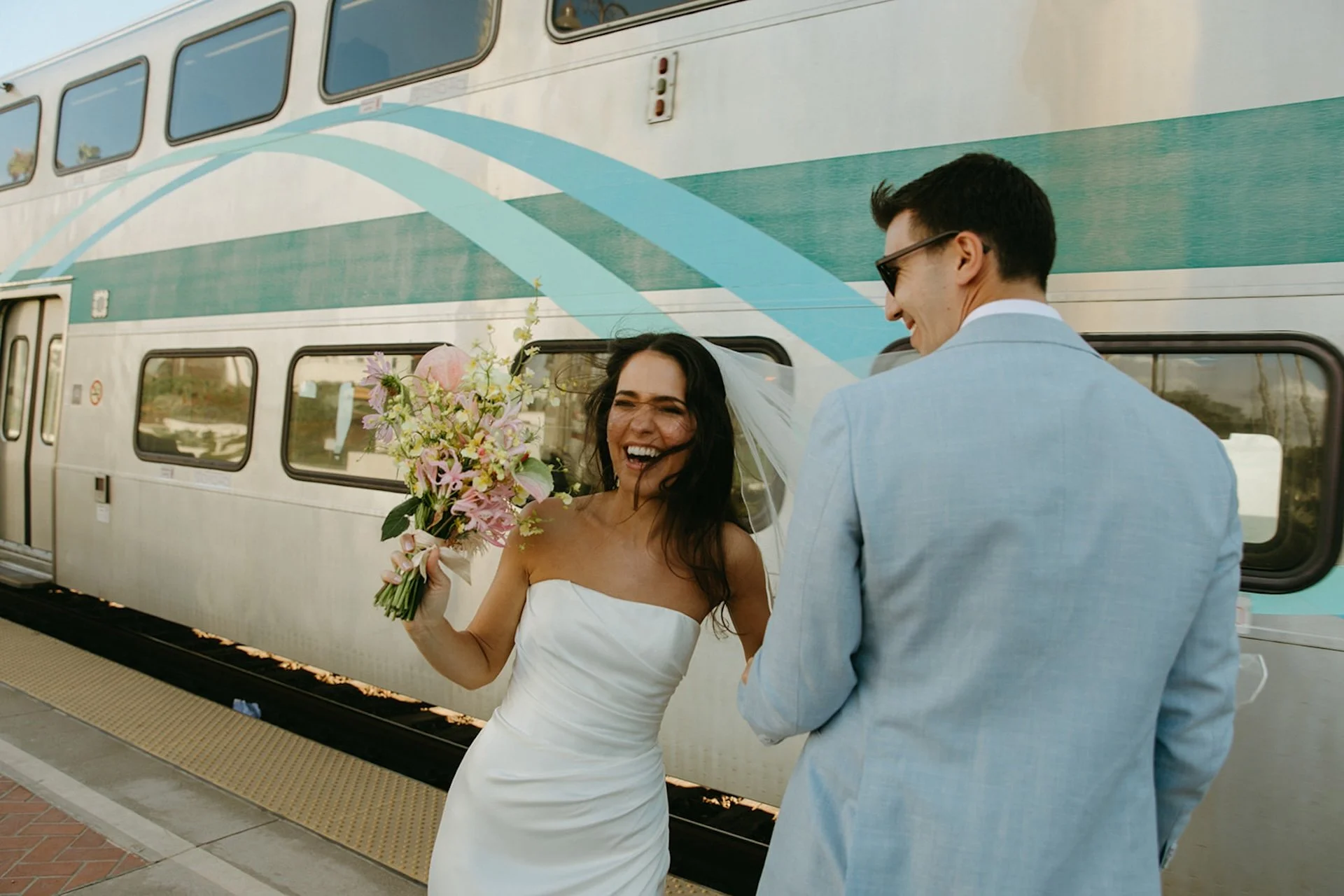 The bride and groom standing on the platform as the frontliner train travels by, blowing the brides hair into her face.