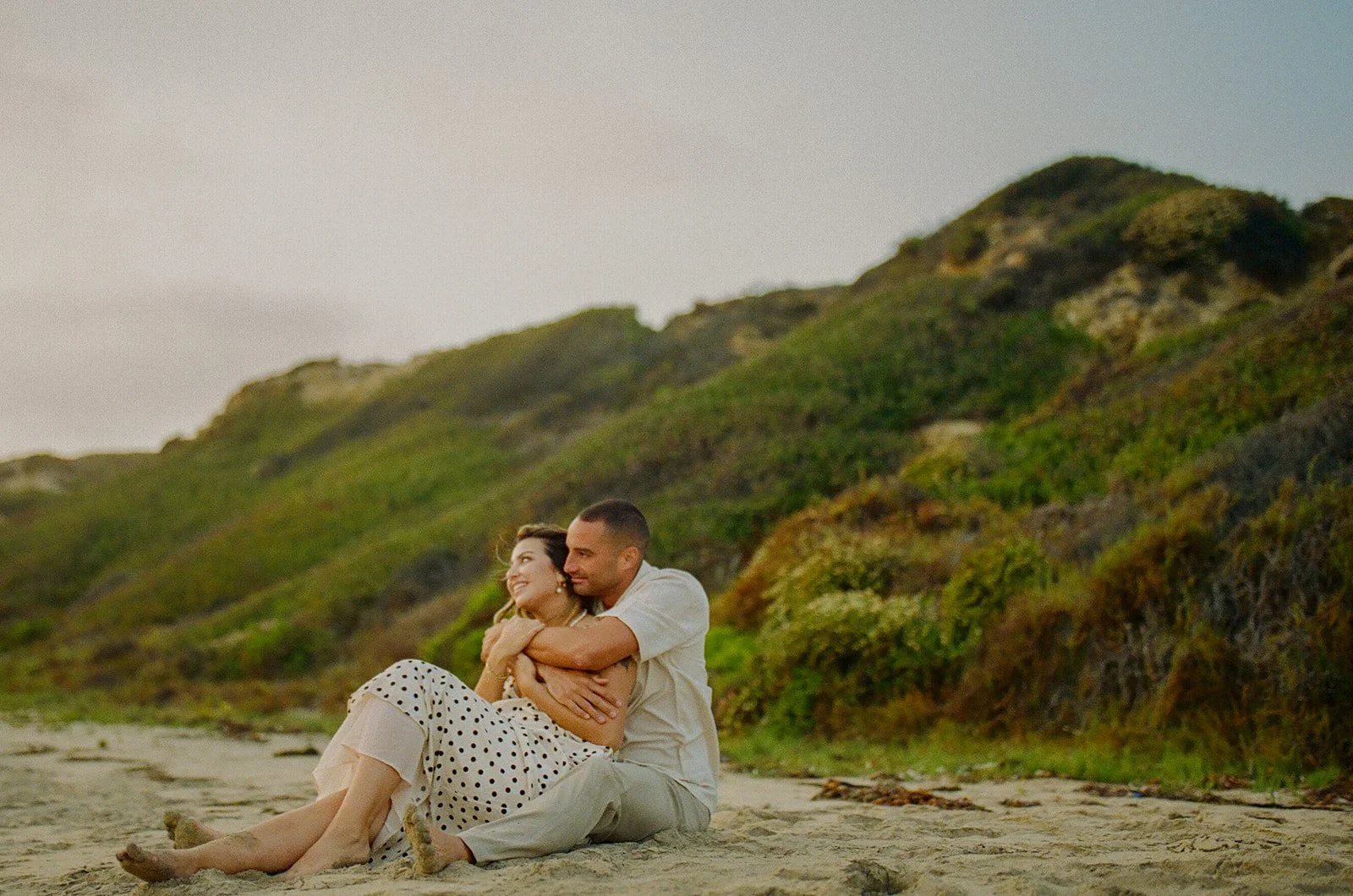 A couple sitting on the beach in beach engagement photo outfits