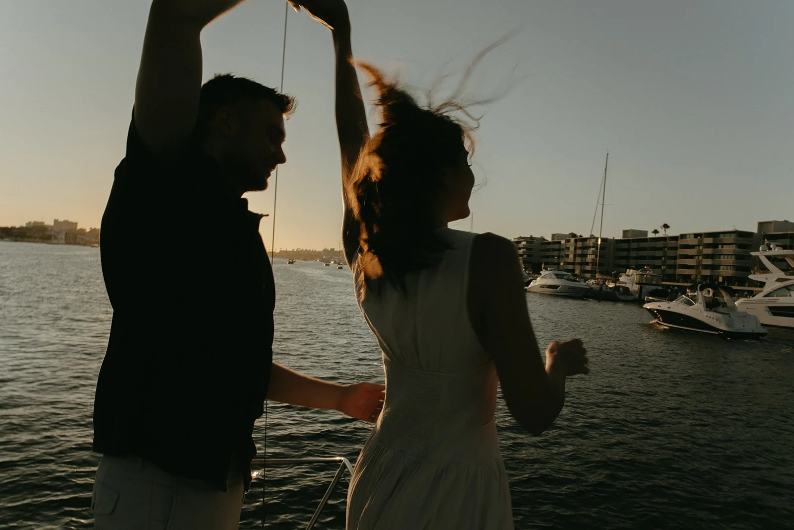 Couple twirling together on a sailboat at dusk, sunset sailboat engagement photos with joyful movement.