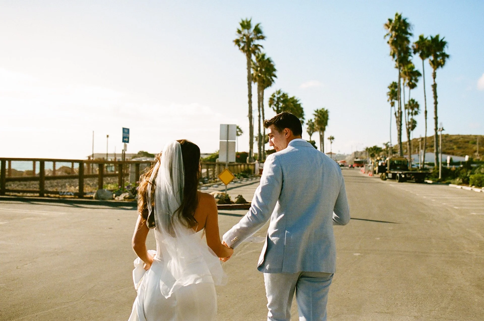 The couple walks hand-in-hand down a palm-lined road, soaking in the coastal sunshine.