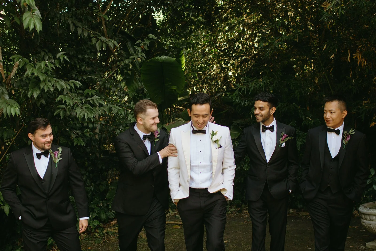 Groom walking with his groomsmen through lush greenery during portraits at a La Venta Inn wedding.