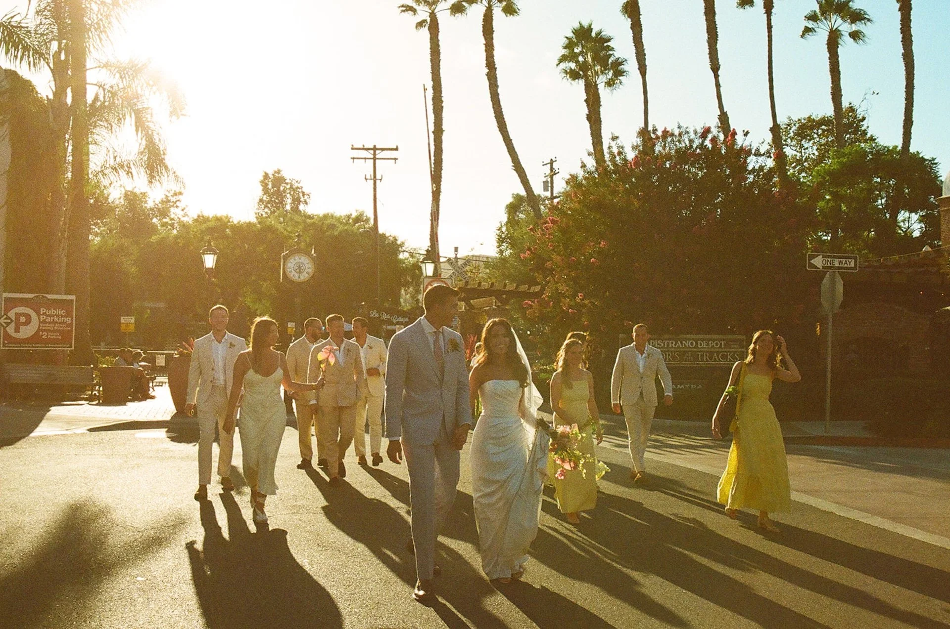 A glowy film photo of the bride, groom, and wedding party walking across the street to their San Juan Capistrano Wedding venue