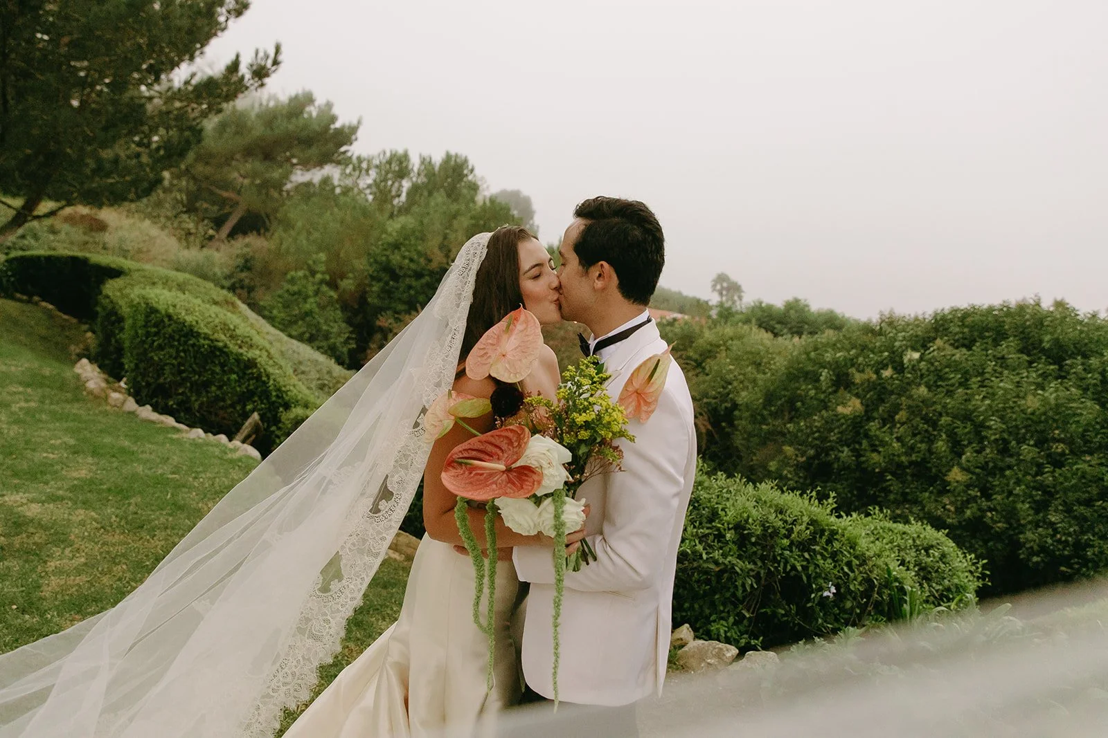 Bride and groom holding each other during portraits with rolling hedges in the background.