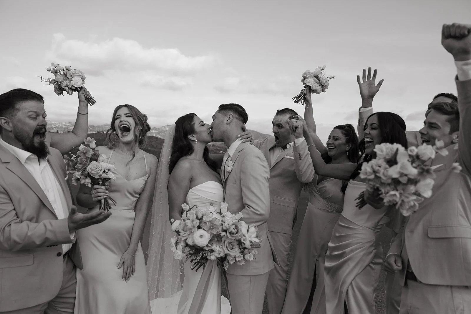 A wedding party cheering while a bride and groom kiss