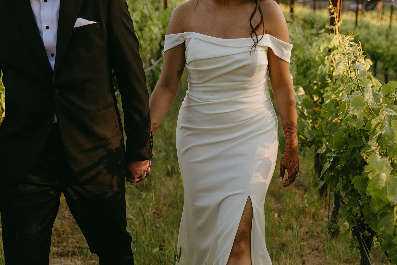 A bride and groom walking through a vineyard