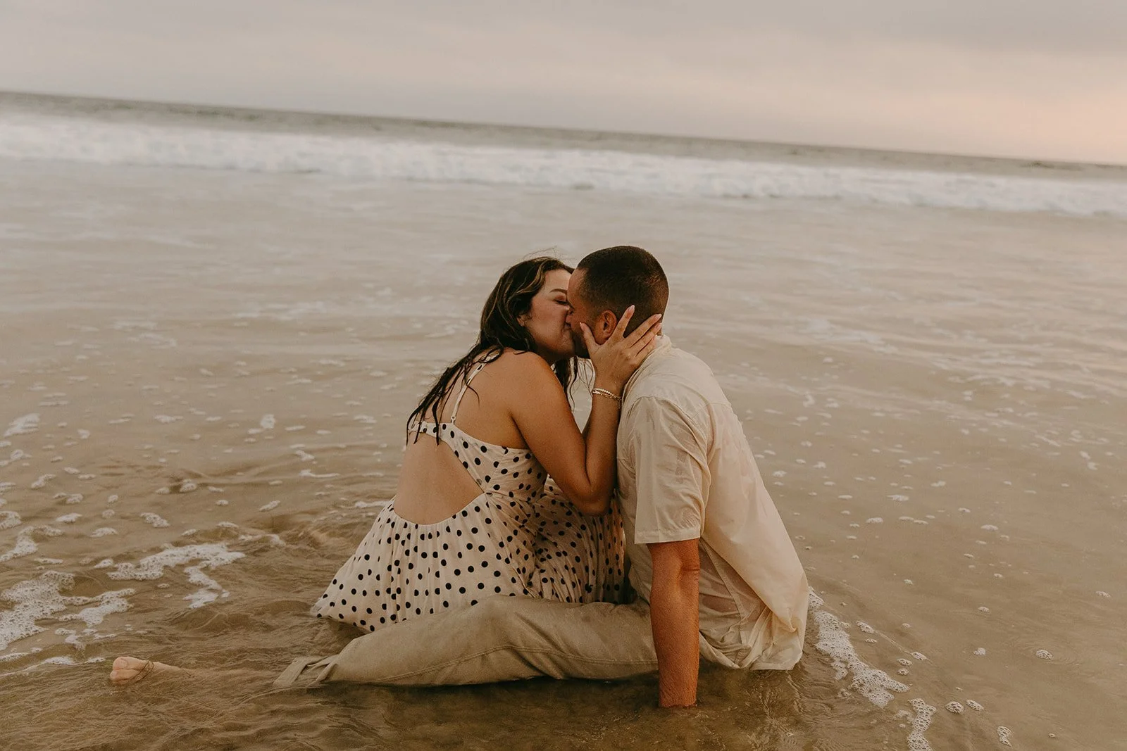 A couple kissing in the ocean while showing what to wear for engagement photos at the beach