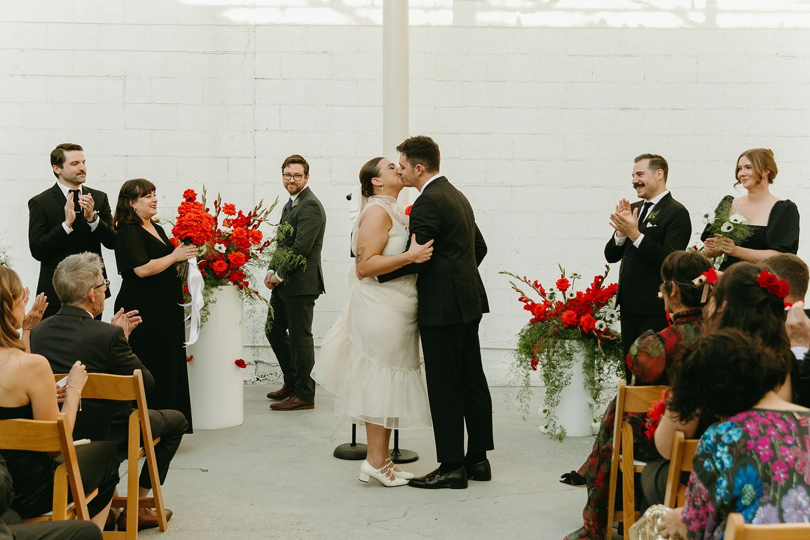 Bride and groom sharing their first kiss as their guests clap around them.