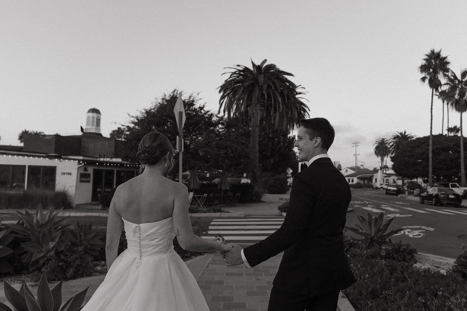Black and white image of the bride and groom walking hand in hand through a charming Southern California street after their ceremony.
