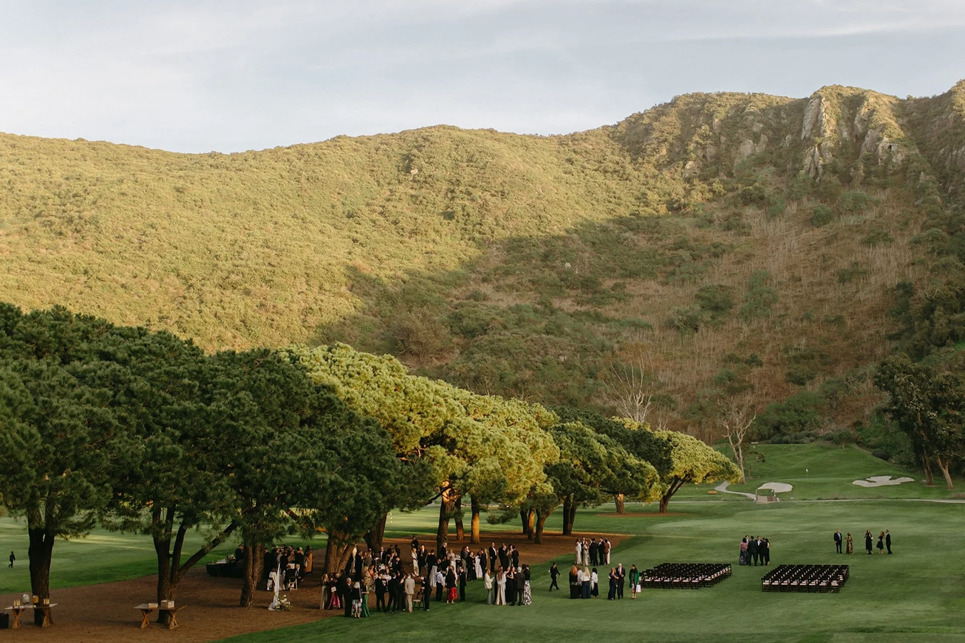 Wide view of wedding guests mingling outdoors surrounded by canyon hills and golden afternoon light.