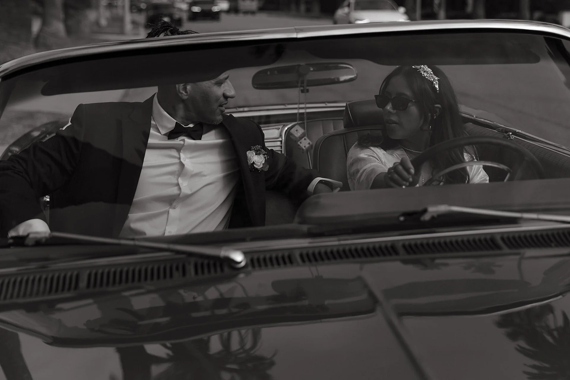 A horizontal photo through the front window of a convertable of the bride and groom sitting in the front seat for some fun wedding portraits.