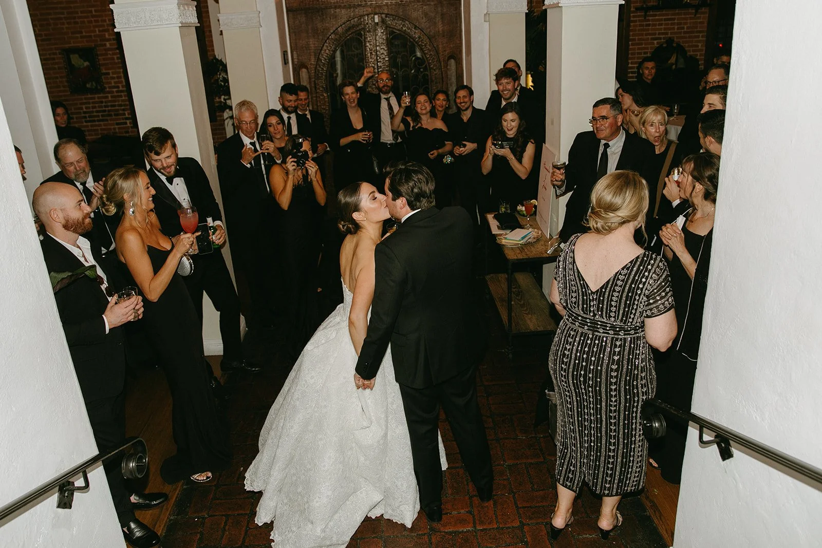 A candid moment of a newly married couple kissing while surrounded by cheering guests during a cocktail hour at one of the stylish DTLA wedding venues.