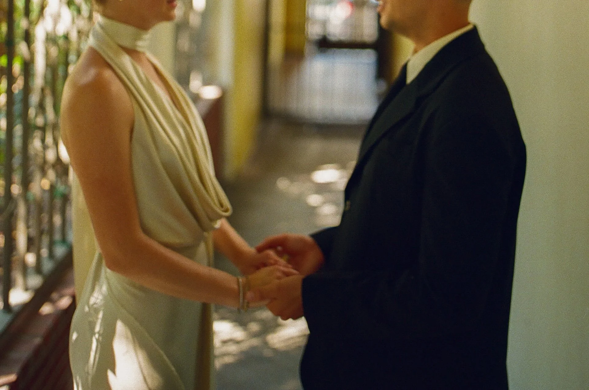 The couple holding hands in a shaded courtyard corridor, with soft natural light and greenery creating an intimate portrait moment.