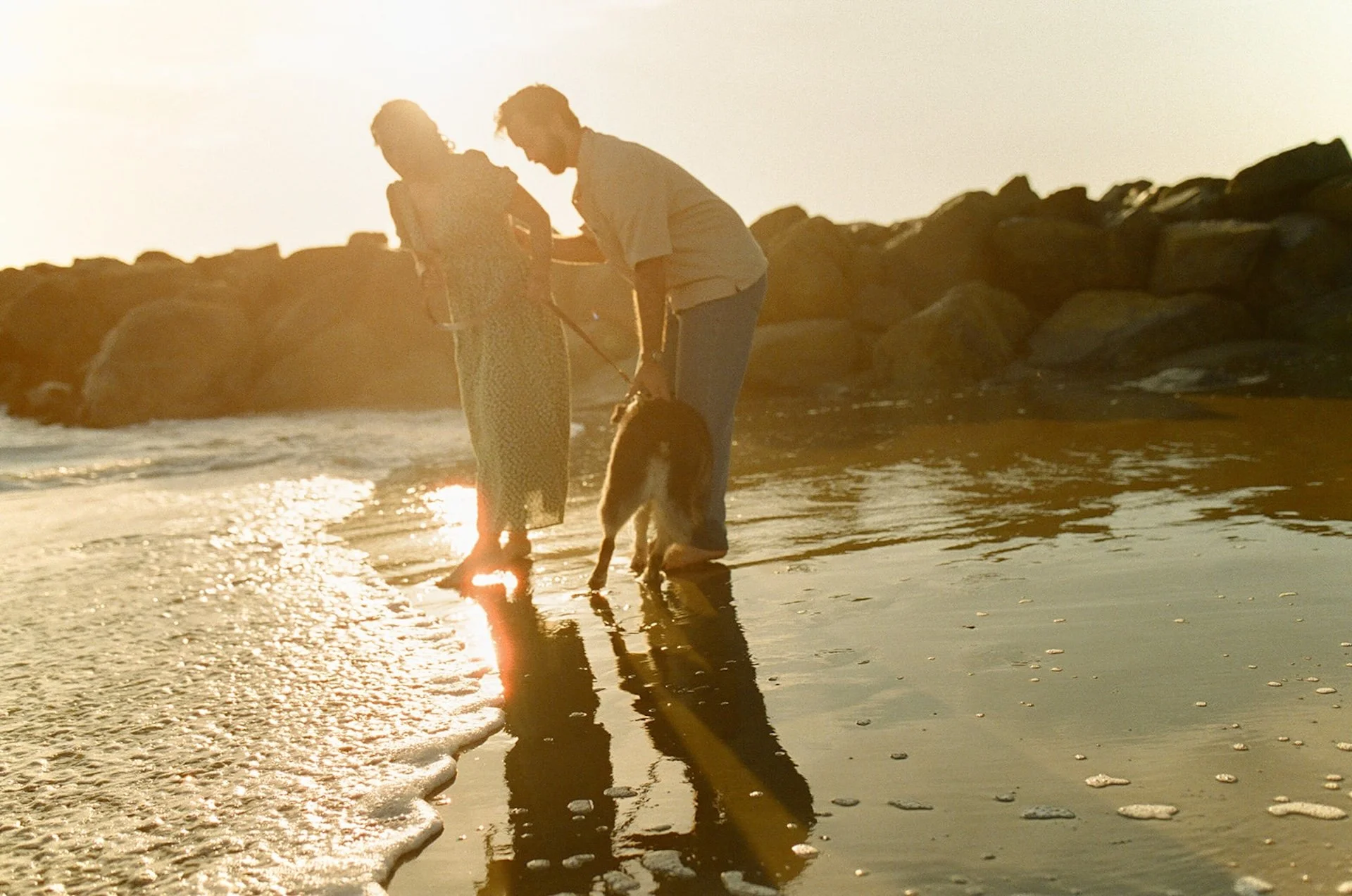 A couple playing on the beach with their dog for a candid photo during their newport beach engagement photos at sunset.