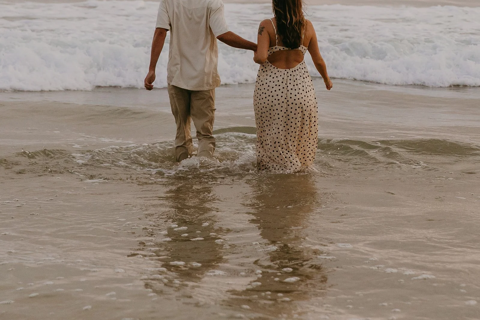 A couple in the ocean in their beach engagement photo outfits