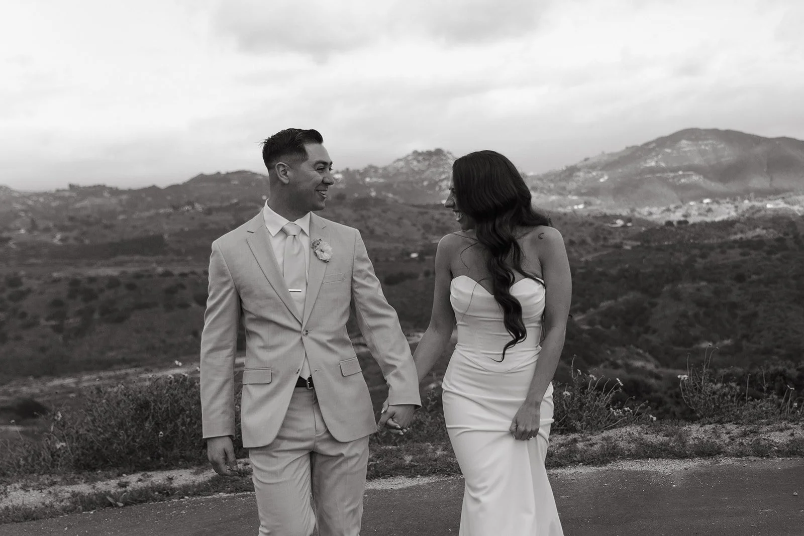 A bride and groom walking towards the camera in front of views at their mountain wedding venue