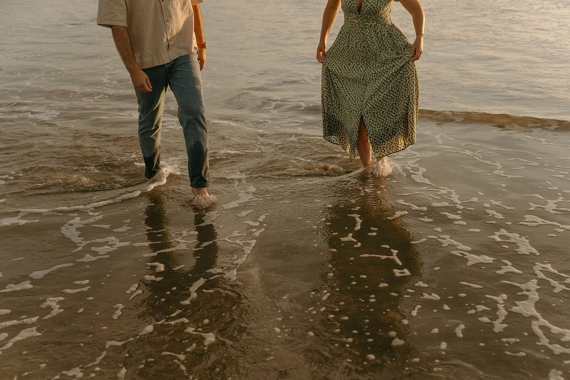 Playful walking shot of a couple splashing through the shoreline during their newport beach engagement photos with foam washing over their feet.