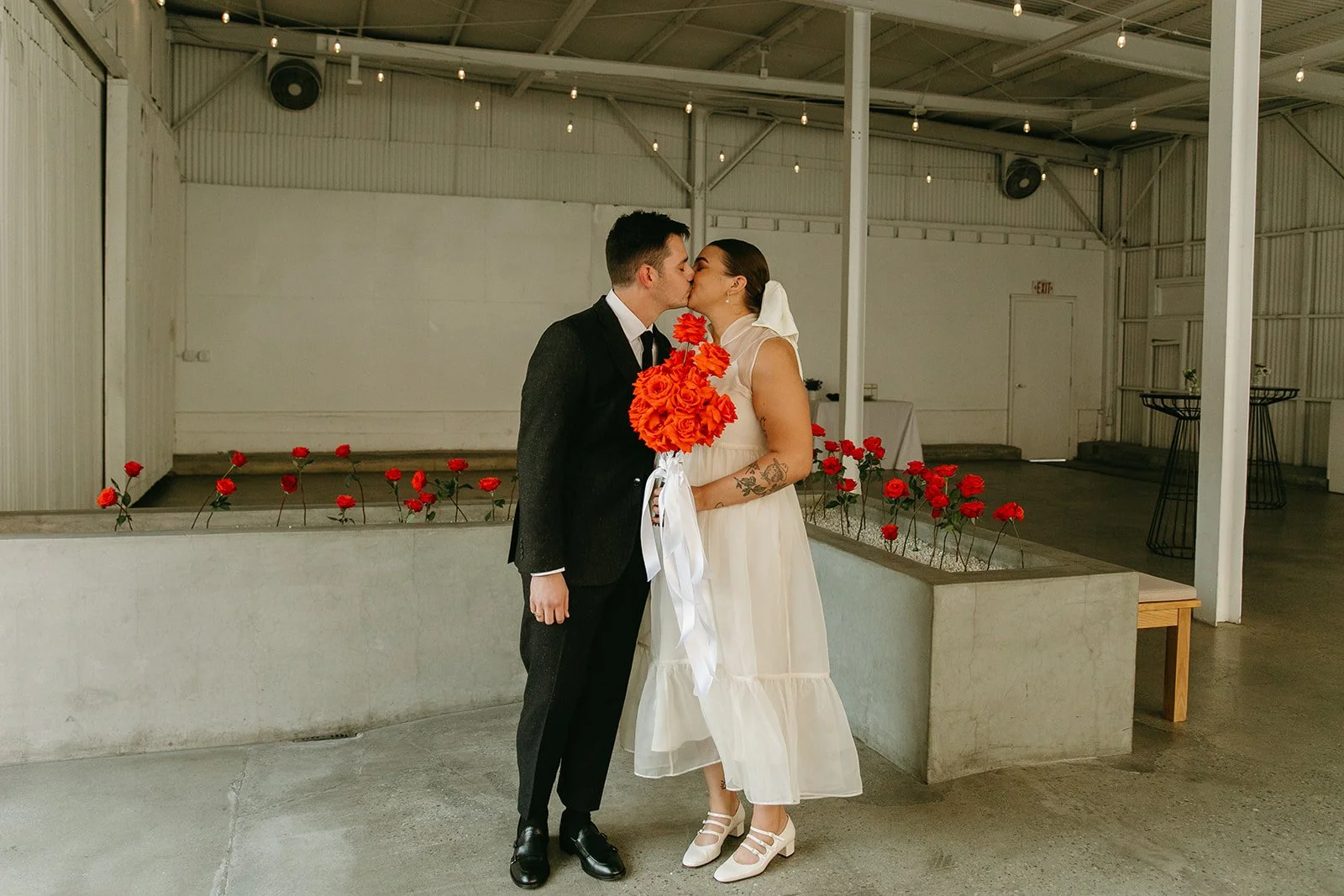 The couple sharing a kiss inside The Revery LA while holding a bright red bouquet, surrounded by minimalist ceremony details.