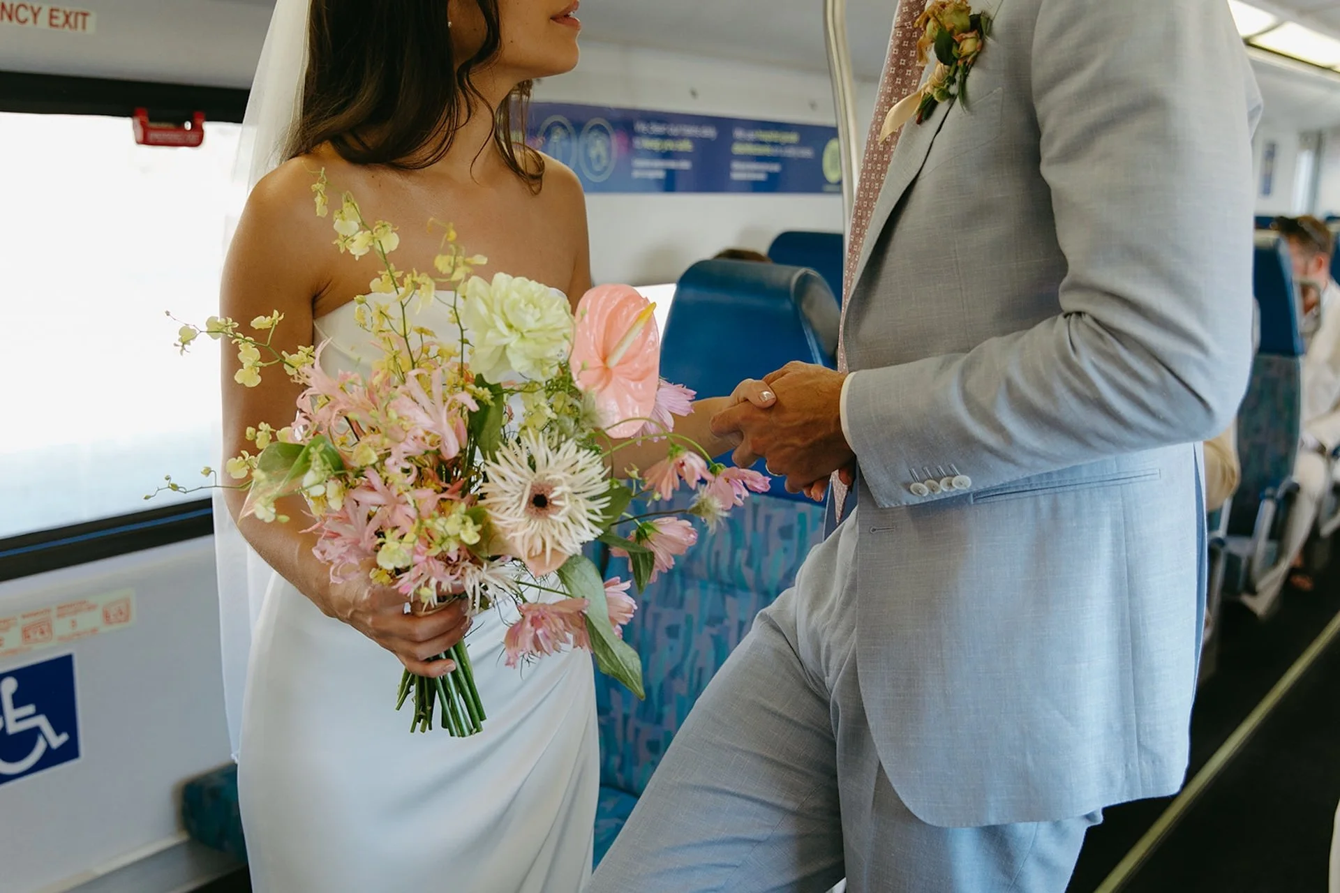 The bride holds a pastel bouquet while riding the train with her groom, creating a candid, modern wedding moment.