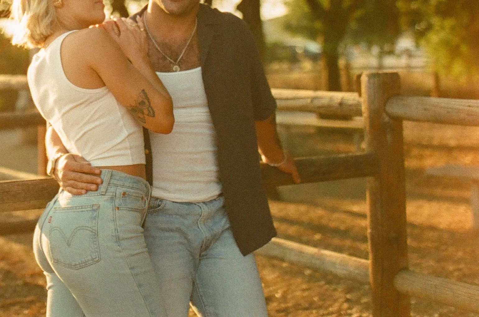 Golden hour film photo of the couple leaning on a fencepost while hugging into each other during their western engagement photos