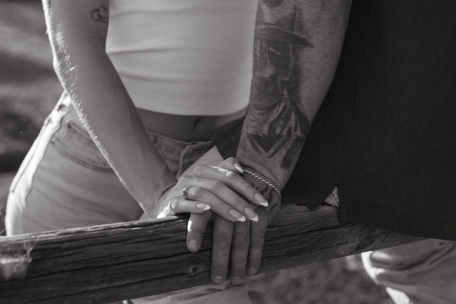 Close up black and white detail shot of the couple’s hands resting on a wooden fence, engagement ring visible.
