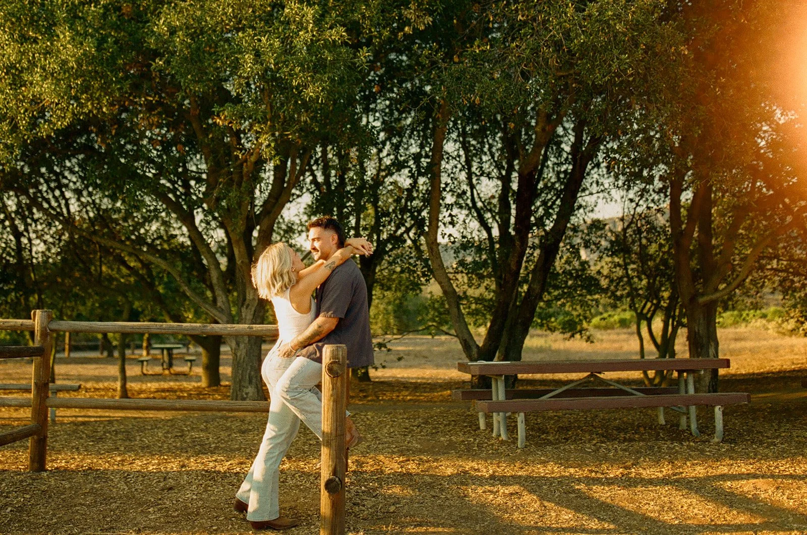 Playful western engagement photos of the couple laughing together in warm golden hour light, leaning into each other in a rustic field setting.